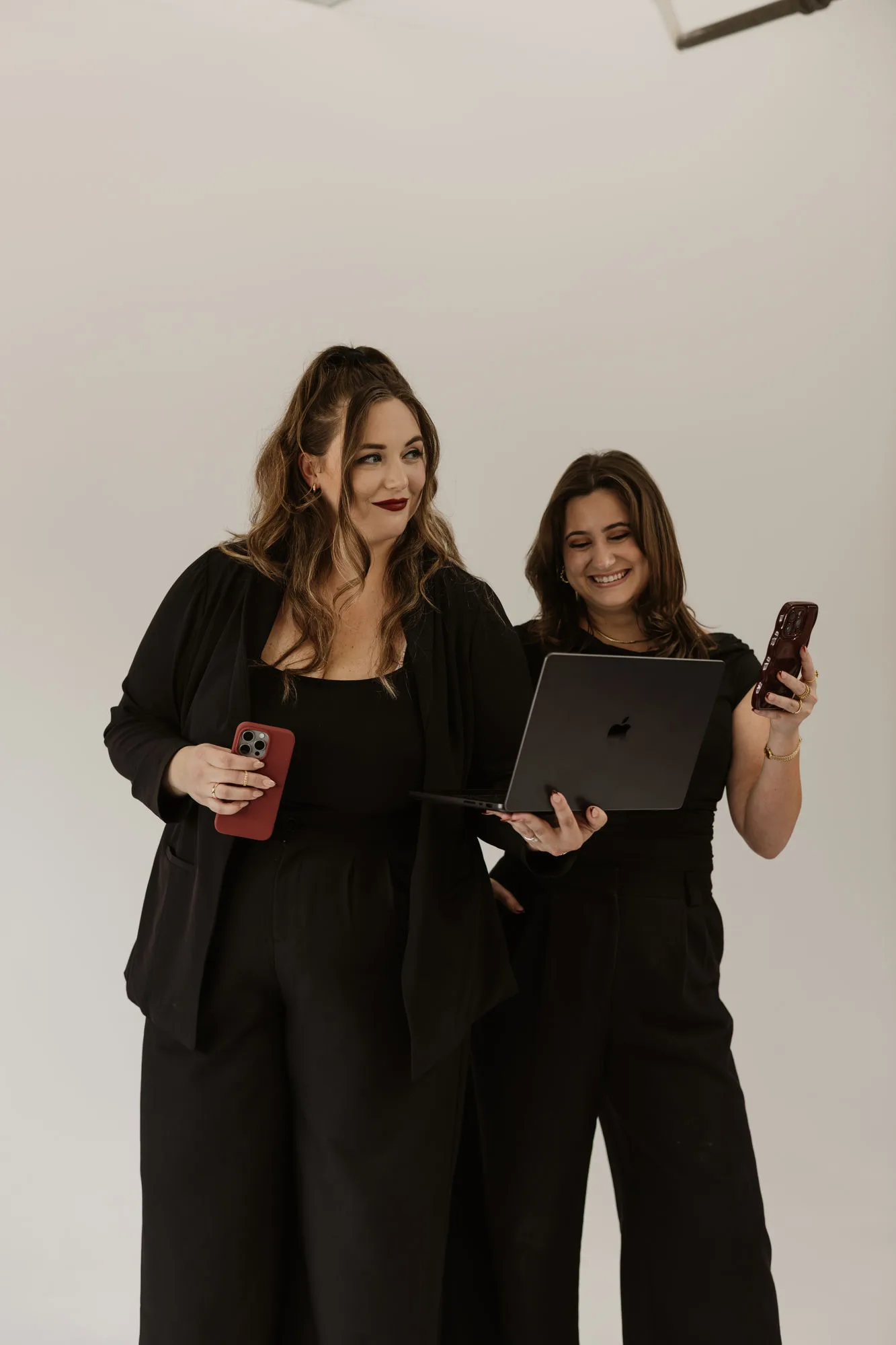 Behind the scenes with The Social Planner founders holding a laptop and phones while creating content