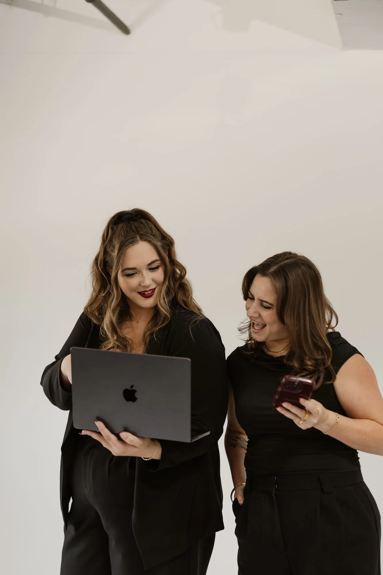The Social Planner founders Tara and Keeley laughing while planning social media content on a laptop and phone